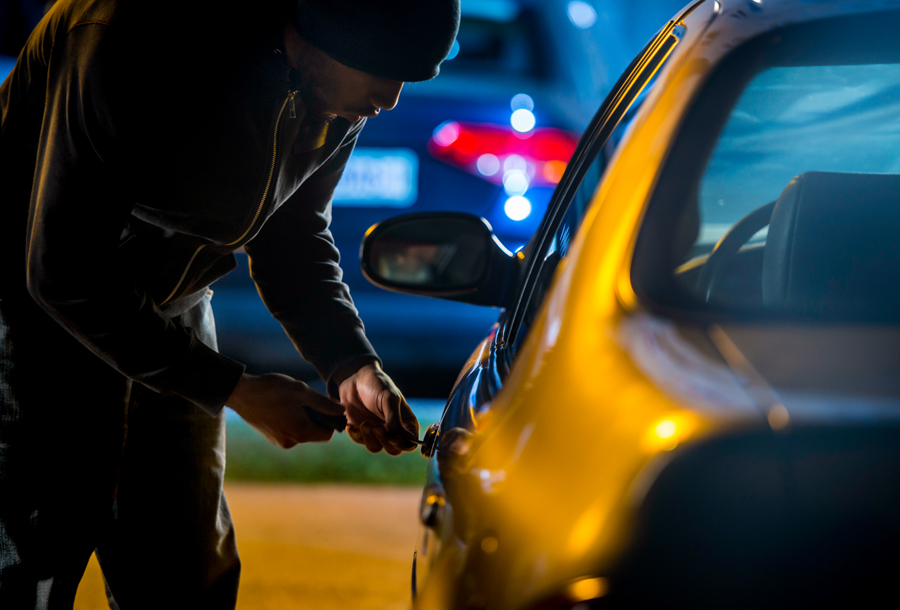 Thief picking a car door lock at night.